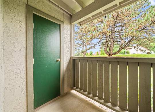 A green door is on the left of a balcony with a view of trees.
