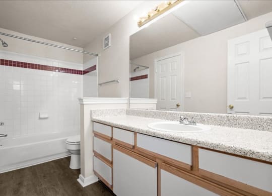 A large bathroom with a shower and bath tub combo and a large vanity mirror with lots of counter space and storage under the sink.