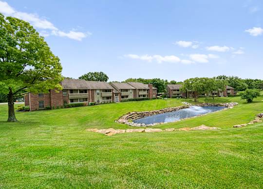 A small pond in the middle of a grassy area with a building in the background.