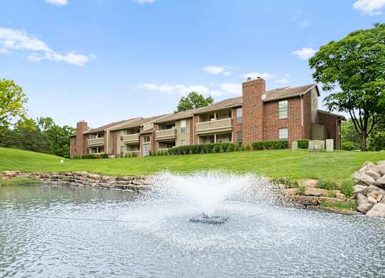 A fountain in the middle of a pond in front of a building.