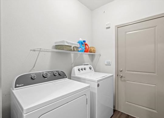 a laundry room with a washer and dryer next to a door at Stonepost Crossing Apartments, Overland Park, 66213