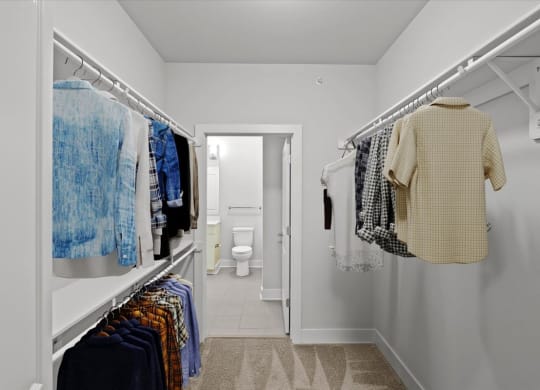 a long white closet with clothes hanging in it and a white bathroom