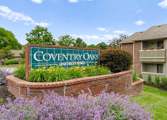 A sign for Coventry Oaks Apartment Homes is surrounded by flowers and greenery.
