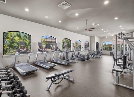 a gym with cardio equipment and windows