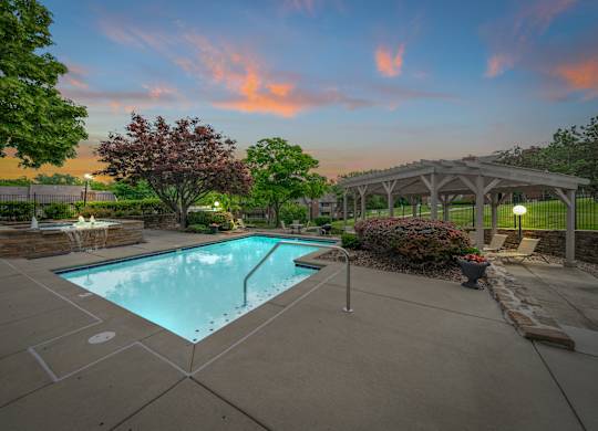 A swimming pool surrounded by a concrete patio and a stone wall with a fountain.