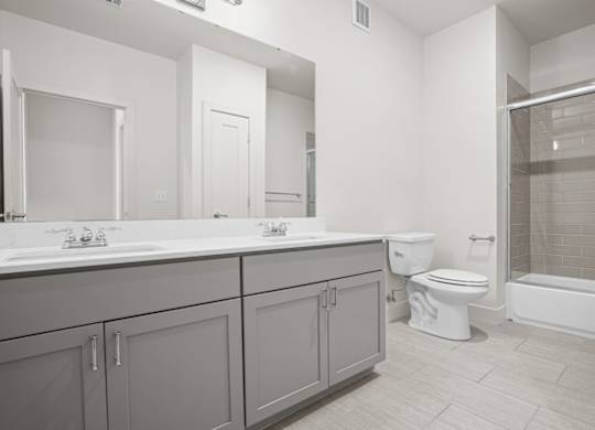 A large bathroom with double vanity sinks, modern finishes, a large mirror, and a sliding glass door shower.