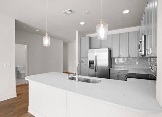 A gourmet kitchen with modern finishes, stainless steel appliances, pendant lighting, and hardwood floors at The Mirabelle Luxury Apartments in KCMO.