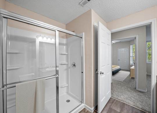 A bathroom with a glass shower door and a white door.at The Claremont Apartment Homes, Overland Park