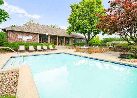 A swimming pool in front of a house with trees.
