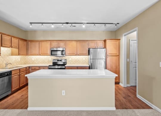 A kitchen with track lighting, quartz countertops, hardwood floors, and stainless steel appliances.