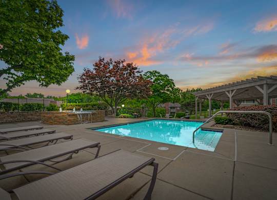 A pool surrounded by trees and lounge chairs.
