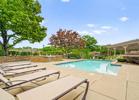 A pool surrounded by trees and chairs.