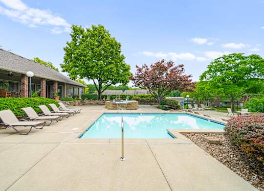 A pool surrounded by trees and chairs in front of a house.