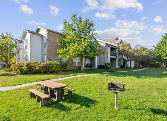 A grassy area with a picnic table and a mailbox in front of apartment buildings. at Crowne Chase Apartment Homes, Overland Park