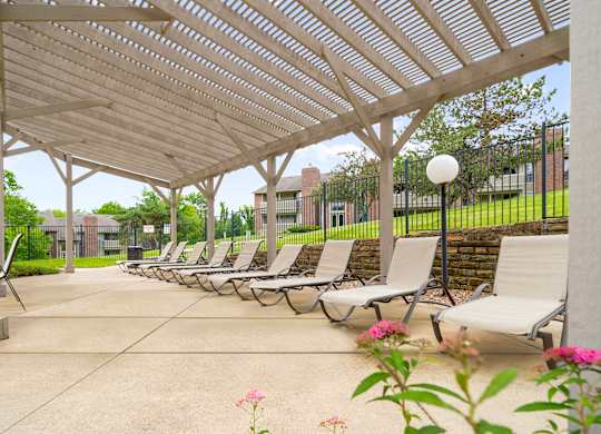 A row of lounge chairs are set up under a white pergola.
