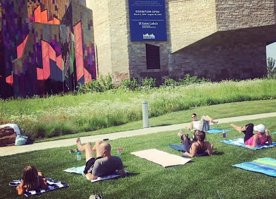A group of people are sitting on the grass in front of a building with a large poster of a brain on it. at Residences at Prairiefire Apartment Homes, Overland Park, Kansas