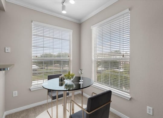 a dining room with two windows and a table with two chairs at The Clairborne Apartment Homes, Grand Prairie, Texas