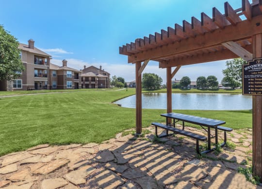 An outdoor gazebo with a picnic table by the lake and green space.
