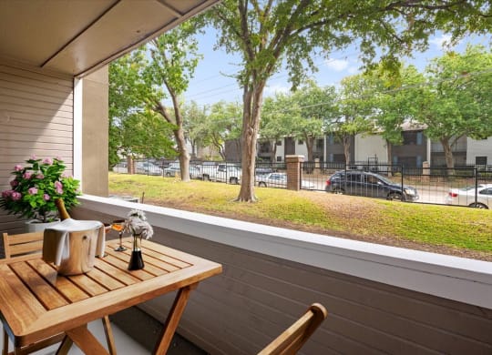 a balcony with a wooden table and two chairs and a large window with a view of a at Creekview Apartment Homes, Dallas, 75254