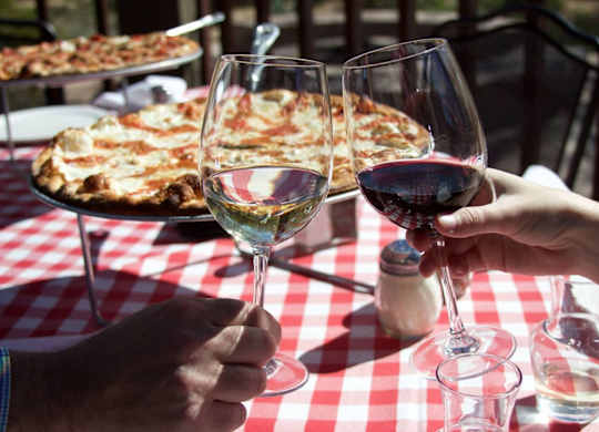 Two people toasting with wine glasses in front of a pizza. at Residences at Prairiefire Apartment Homes, Overland Park, 66223