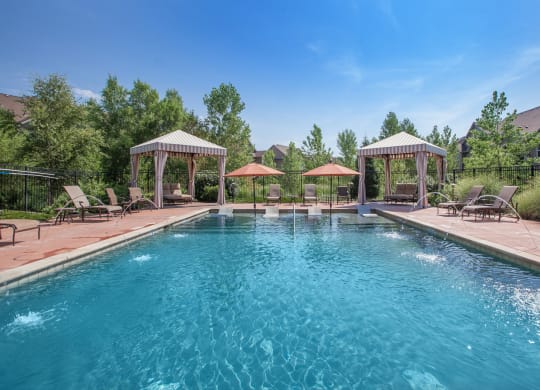A beautiful clean saltwater pool with shaded lounge seating, fountains, and two cabanas.