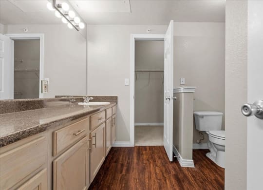 a bathroom with a toilet sink and mirror at The Clairborne Apartment Homes, Grand Prairie, TX