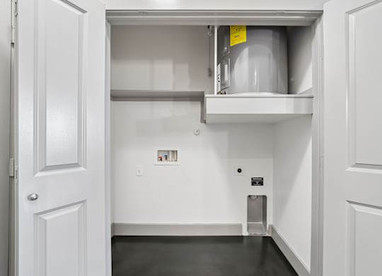 A white door is open to a small storage room with a shelf and a container.