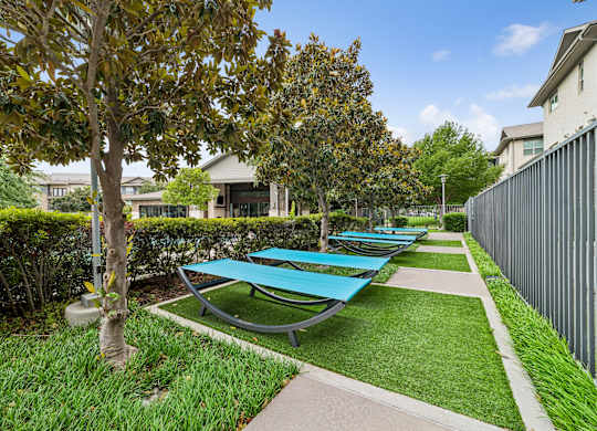 A row of blue sun loungers are lined up on a green lawn.