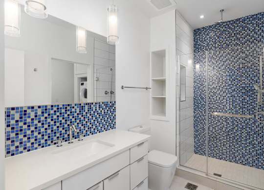A bathroom with a blue tiled shower and white countertop.