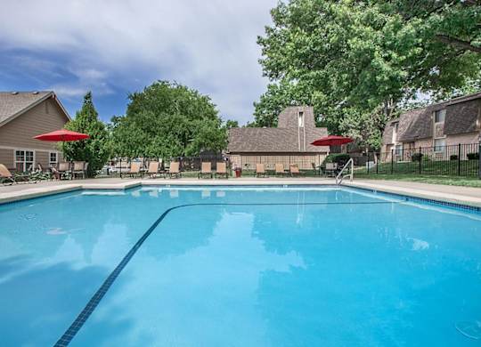 A clean outdoor swimming pool with trees and lounge seating.