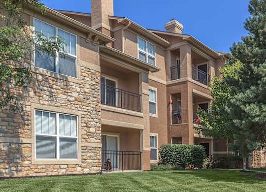 The exterior of an apartment building overlooking a lush green space and tree