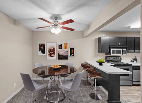 A dining room with a ceiling fan next to a modern kitchen.