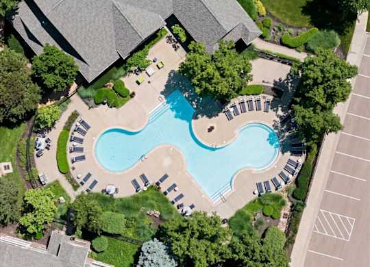 An aerial view of a swimming pool surrounded by trees and a parking lot.
