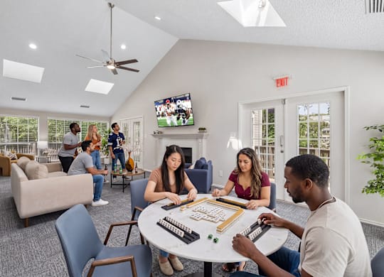 A group of people playing a board game in a room with a TV screen on the wall.