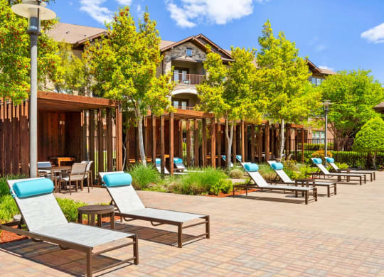 a patio with lounge chairs and tables and a building in the background