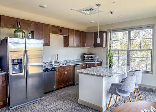 Modern kitchen in rooftop lounge at The Dorset Apartments with stainless steel appliances, granite countertops, and island seating.