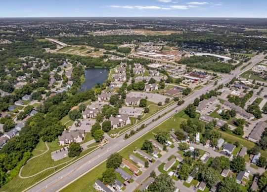Elevated drone view of Millcreek Woods Apartment Homes in Olathe, Kansas, showcasing residential buildings, surrounding neighborhoods, mature trees, and nearby roadways.