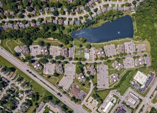 Top-down aerial view of Millcreek Woods Apartment Homes featuring apartment buildings, parking areas, landscaped grounds, and the community lake.