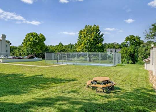 Outdoor basketball court surrounded by green lawn and mature trees at Millcreek Woods Apartment Homes.