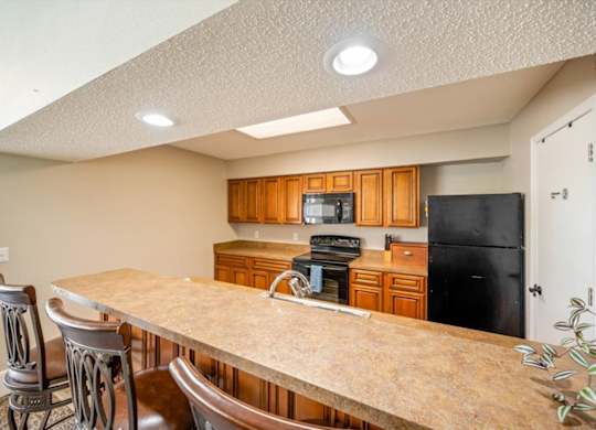 Clubhouse kitchen featuring wood cabinetry, black appliances, and breakfast bar seating.
