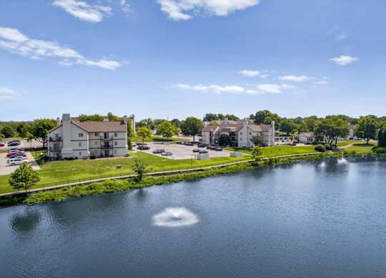 Decorative fountain in the community lake with apartment homes and mature trees nearby.