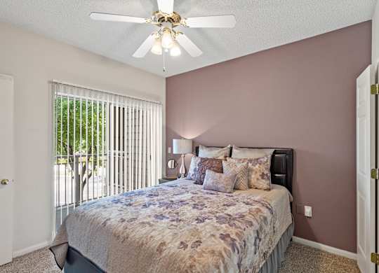 A bedroom with a ceiling fan and sliding glass door patio.