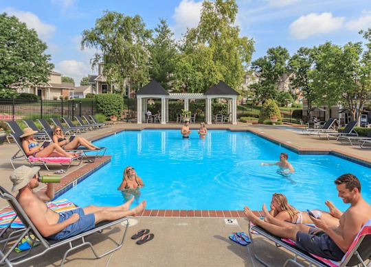 People are relaxing by the pool on a sunny day.