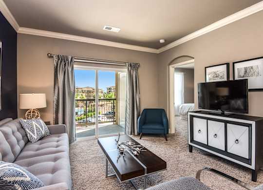 A living room with a grey sofa, a black and white cabinet, a coffee table, and a television. at Residences at Prairiefire Apartment Homes, Overland Park, KS
