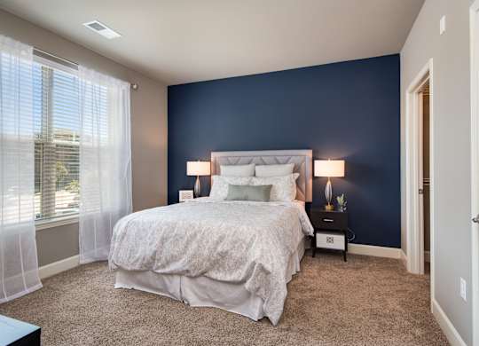 A bedroom with a large bed and a window with curtains. at Residences at Prairiefire Apartment Homes, Overland Park, 66223