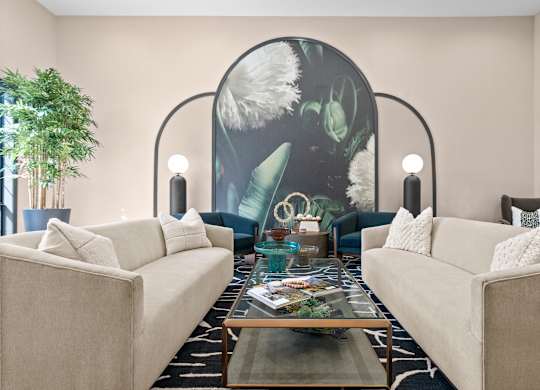 A living room with two beige couches, a glass coffee table, and a large mural on the wall.