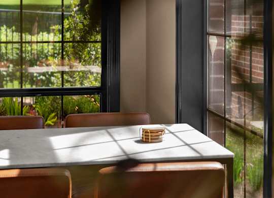 A table with a basket on it is in front of a window with a view of a garden.