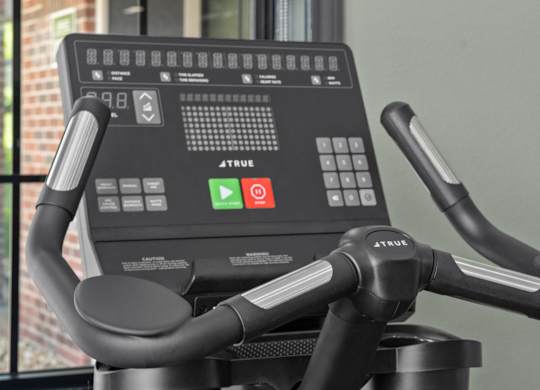 A close up of a True bike workout machine with a digital screen and handlebars.