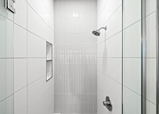 A white tiled shower with a glass door and a silver handle.