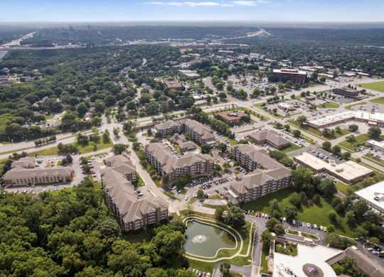 Aerial view of The Claremont Apartments community showcasing residential buildings, a scenic pond, and nearby Overland Park, Kansas neighborhoods.